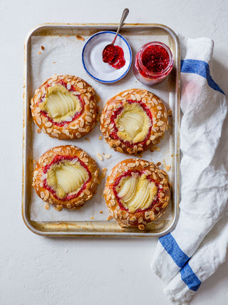 Pear & Raspberry Jam Brioche Tarts topped with sliced pears, almond flakes, served with raspberry jam on the side.