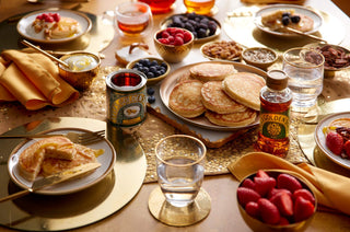 A table set with homemade pancakes, Lyle's Golden Syrup 700g Pouring Bottle and 454g Tin, berries, and nuts on an absolutely golden tablecloth.