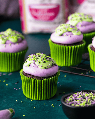 Halloween Chocolate cupcakes with purple frosting and green sprinkles on a teal surface.