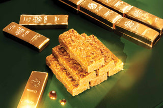 A stack of Lyle's Golden Syrup Flapjacks on a green surface with shiny gold bars in the background.