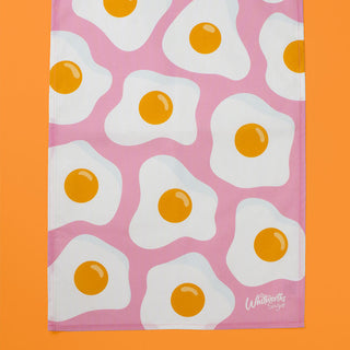 Tea towel with fried egg pattern on a pink background