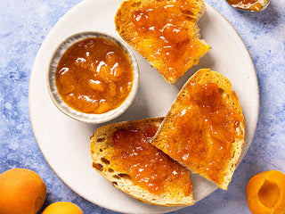 Homemade apricot jam on toast, surrounded by a jam jar and fresh apricots