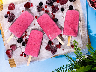 4 red summer ice lollies and frozen berries laid flat on a wooden board