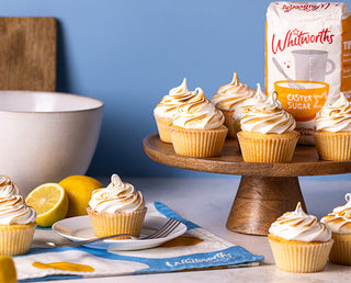 A cake stand filled with lemon meringue cupcakes next to a bag of Whitworths caster sugar