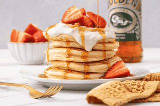 Pancake stack topped with yogurt, strawberry and a drizzle of golden syrup