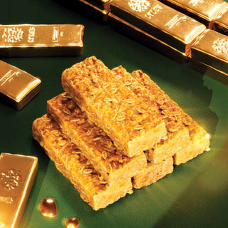 A stack of Lyle's Golden Syrup Flapjacks on a green surface with shiny gold bars in the background. 