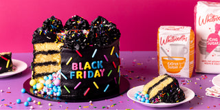 Black Friday cake with colorful sprinkles and a slice on a plate, against a pink background.