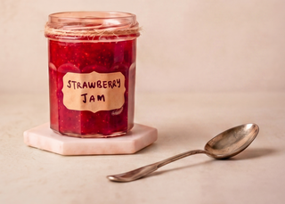 Jar of strawberry jam with a spoon on a beige background, featuring the text 'Spread the Love' and the Sugar & Syrup logo.