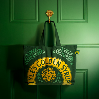 Tote bag with Lyles Golden Syrup design hanging on a green door.