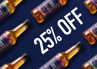 Promotional graphic for a summer syrup sale showing multiple bottles of Ezeley Parishta Barista Syrup arranged diagonally on a dark blue background with large white text reading '25% OFF' and a 'SUGAR + SYRUP.COM' logo in the bottom right.