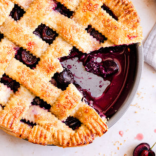 A cherry pie with a golden lattice crust, showing a slice taken out. 
