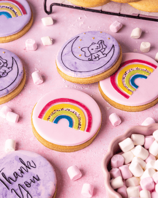 Colorful cookies with rainbow and moon designs on a pink background with marshmallows.