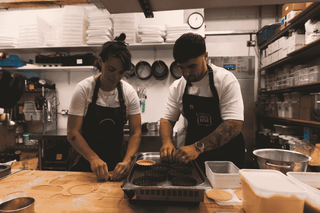 Two chefs working in a kitchen with various utensils and equipment around them.