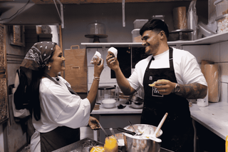 Two chefs in a kitchen holding up pastry, smiling.